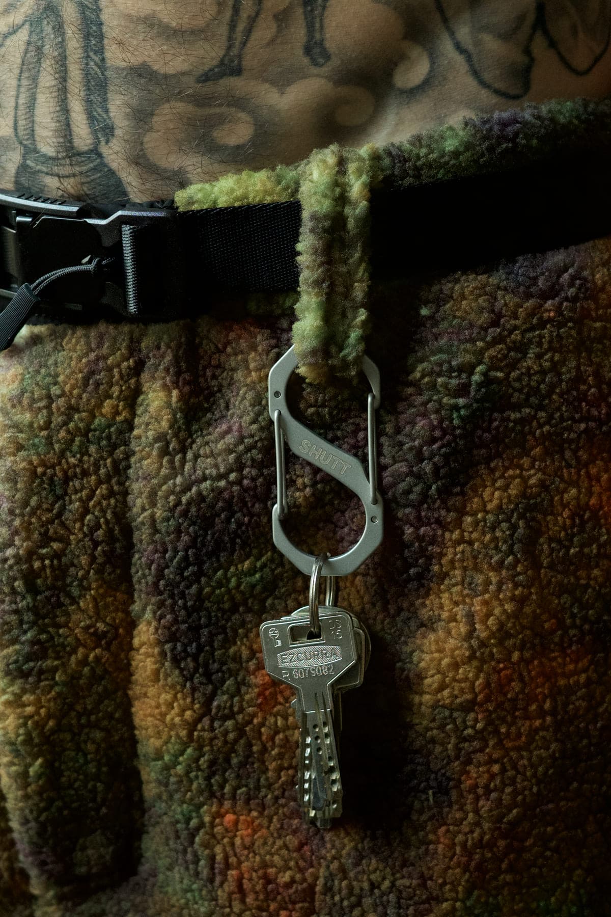 S-CARABINER clipped to a camo fleece belt loop, SHUTT engraving and a key